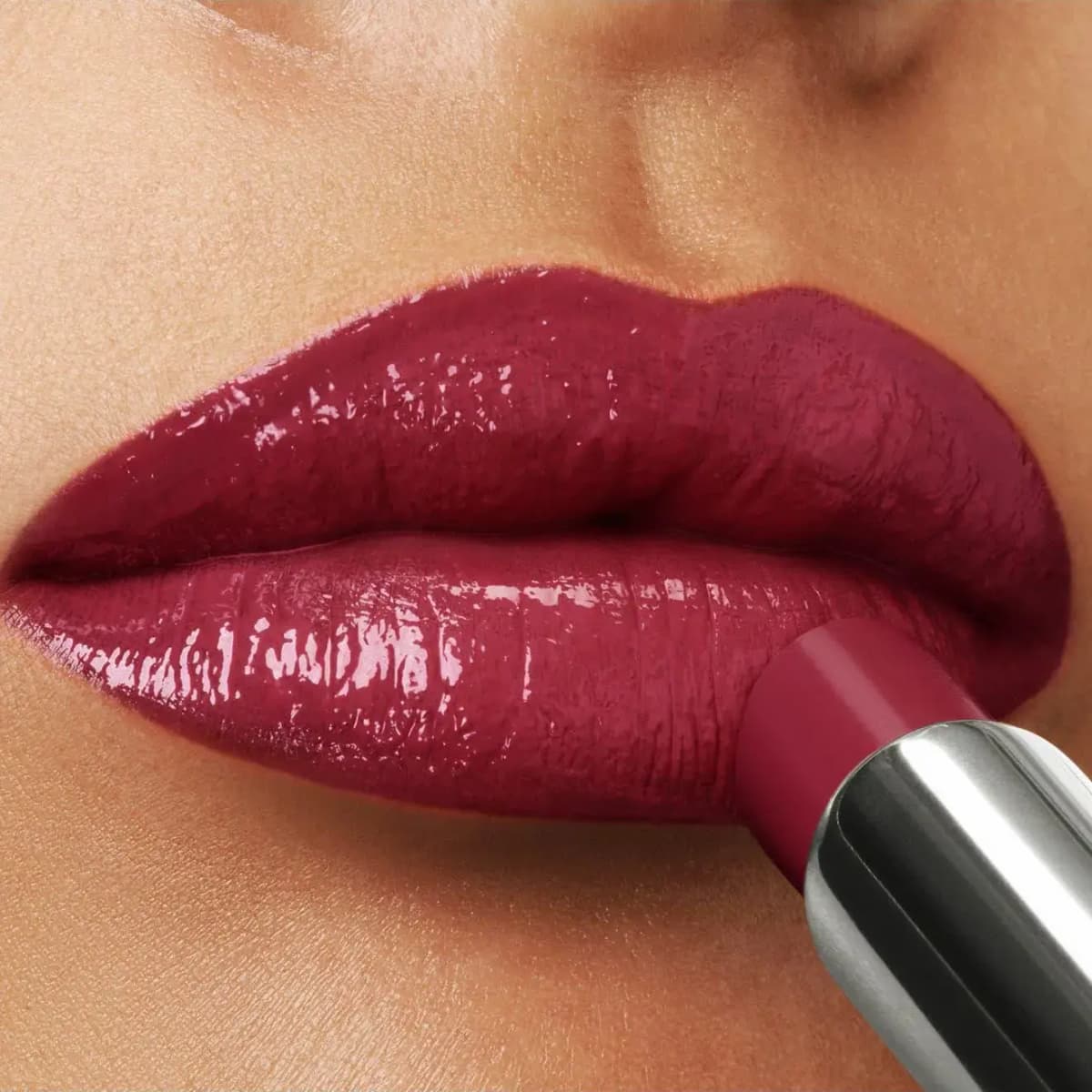 Glossy, high-shine berry lipstick being applied to lips on a light-medium skin tone