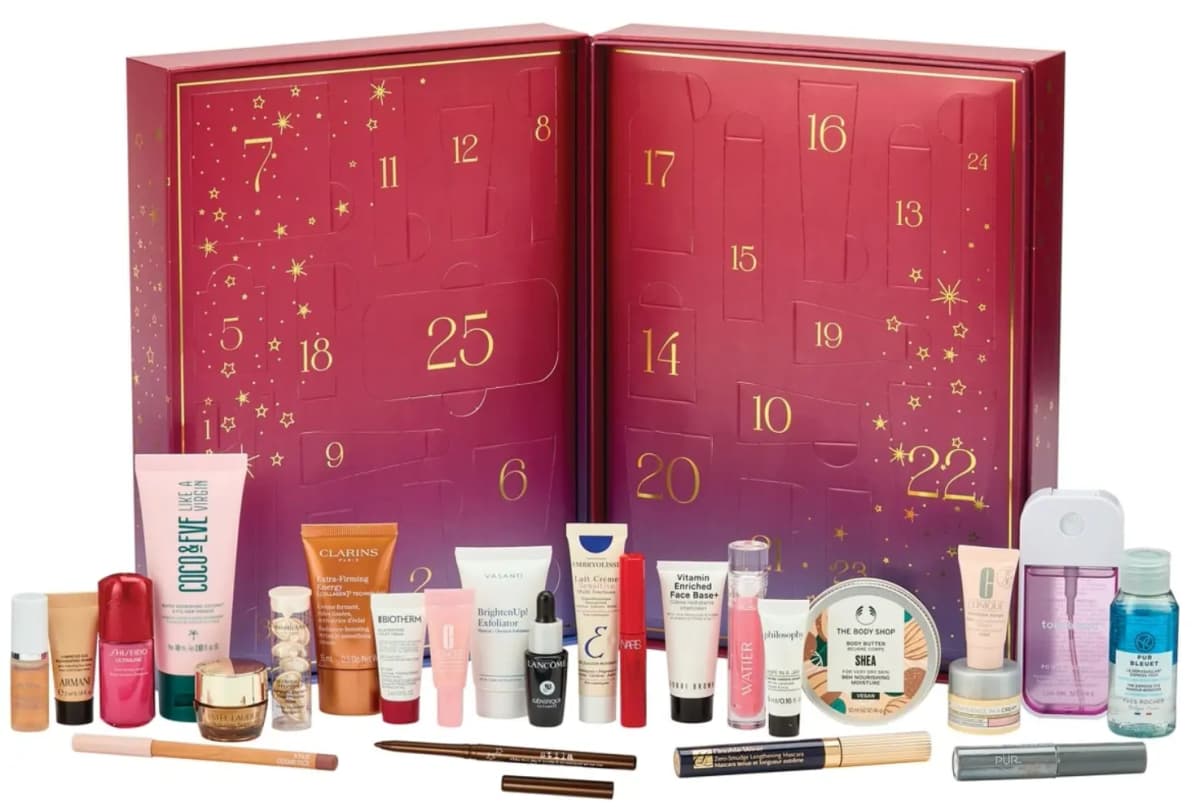 Open burgundy advent calendar book with gold numbered doors and beauty products arranged in front including creams