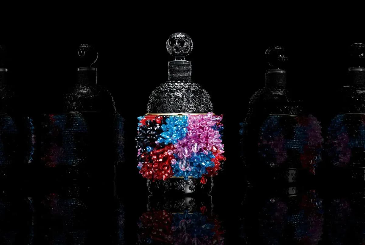 Beaded black Bee Bottle lit centre stage among shadowy bottles, reflected on a glossy black surface