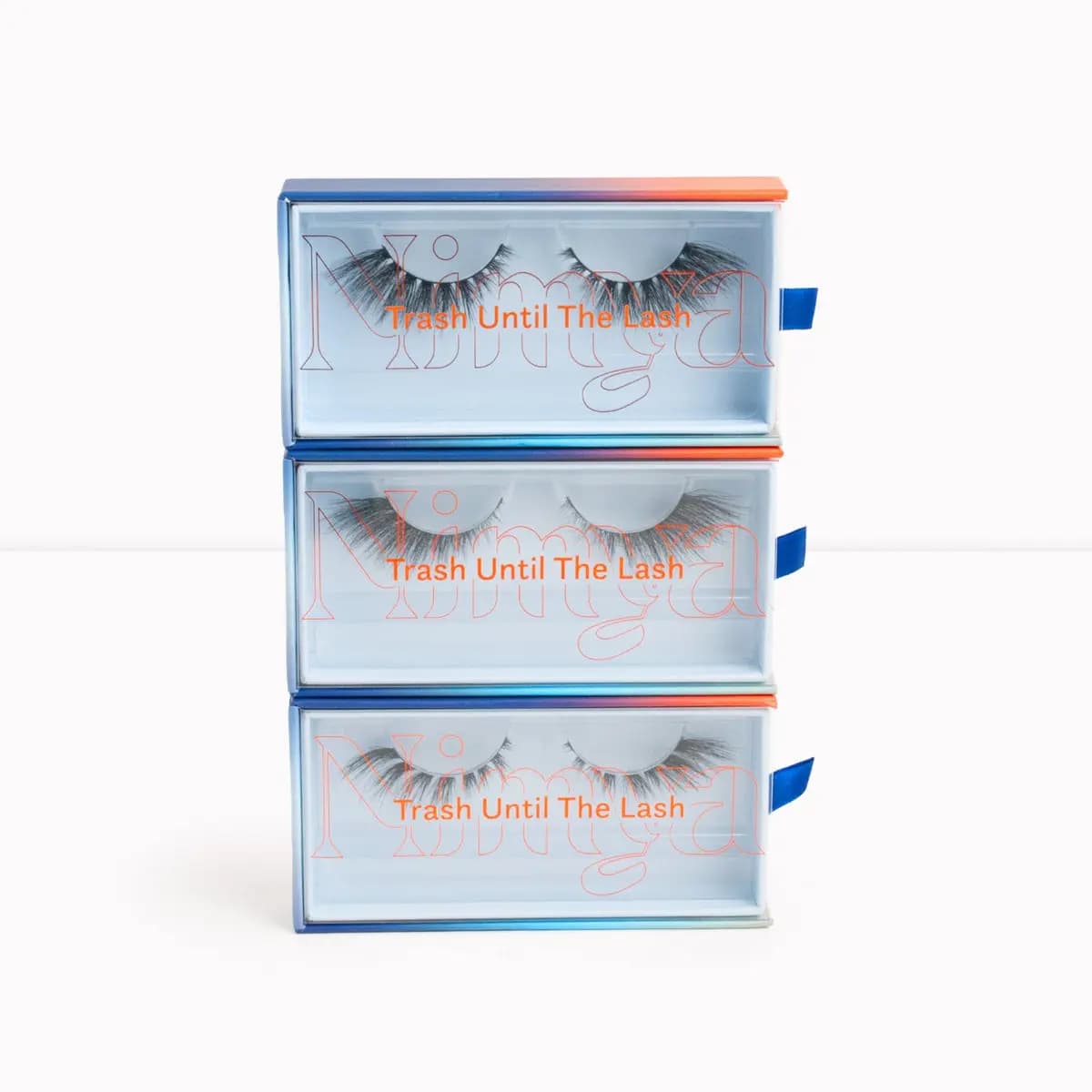 Stack of three blue-and-orange Nimya lash boxes labeled 'Trash Until The Lash' with lashes visible through clear windows.