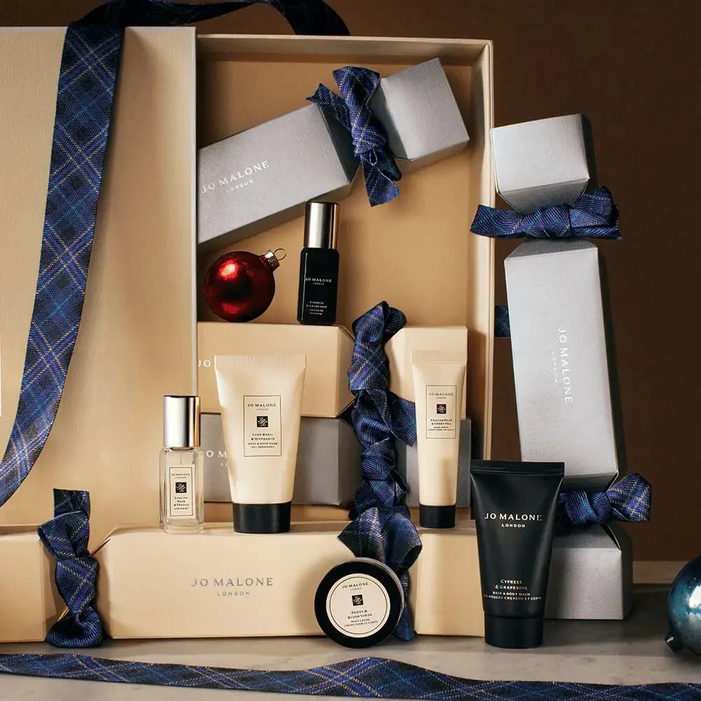 Cream and silver cracker boxes with navy tartan ribbons surrounded by minis, washes, body crème and a red bauble