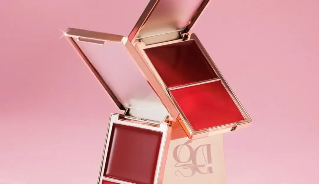 Two open rose-gold compacts in deep berry and crimson cream blush, stacked at angles on a pink background