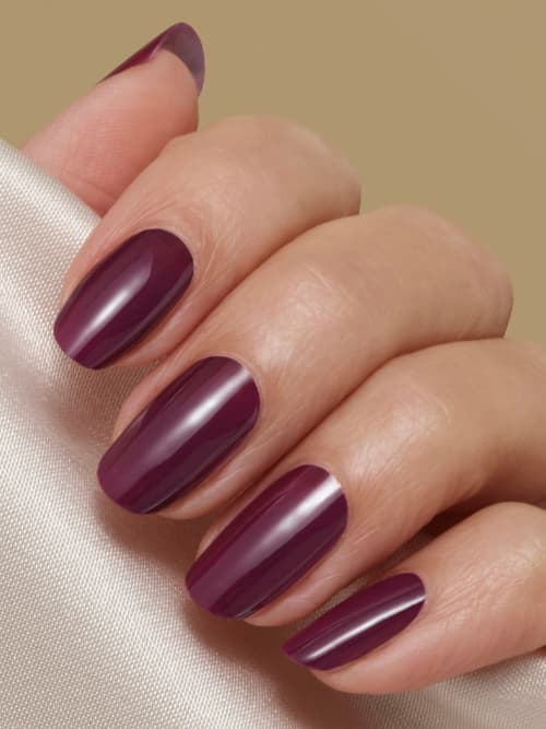 Hand with glossy deep plum oval nails resting on champagne satin against a beige backdrop