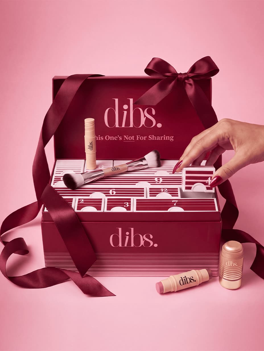 DIBS Beauty 12 Days of DIBS Advent Calendar open on pink, hand lifting door 4, with brush, sticks and burgundy satin bow