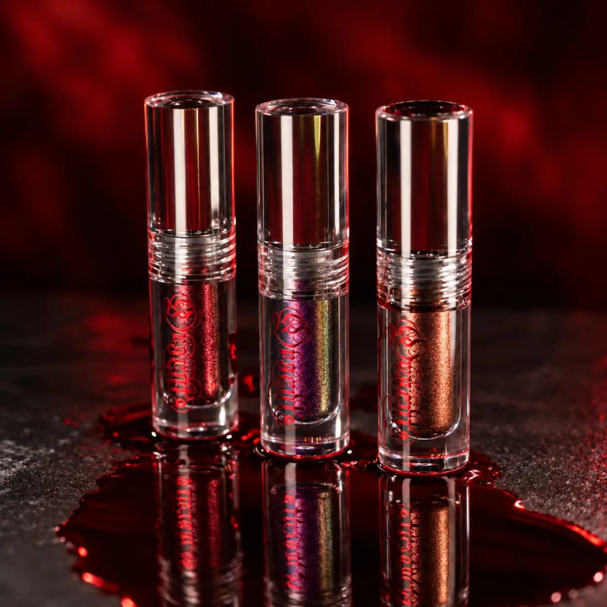 Three clear liquid eyeshadow tubes in red, iridescent purple and copper standing in a pool of fake blood