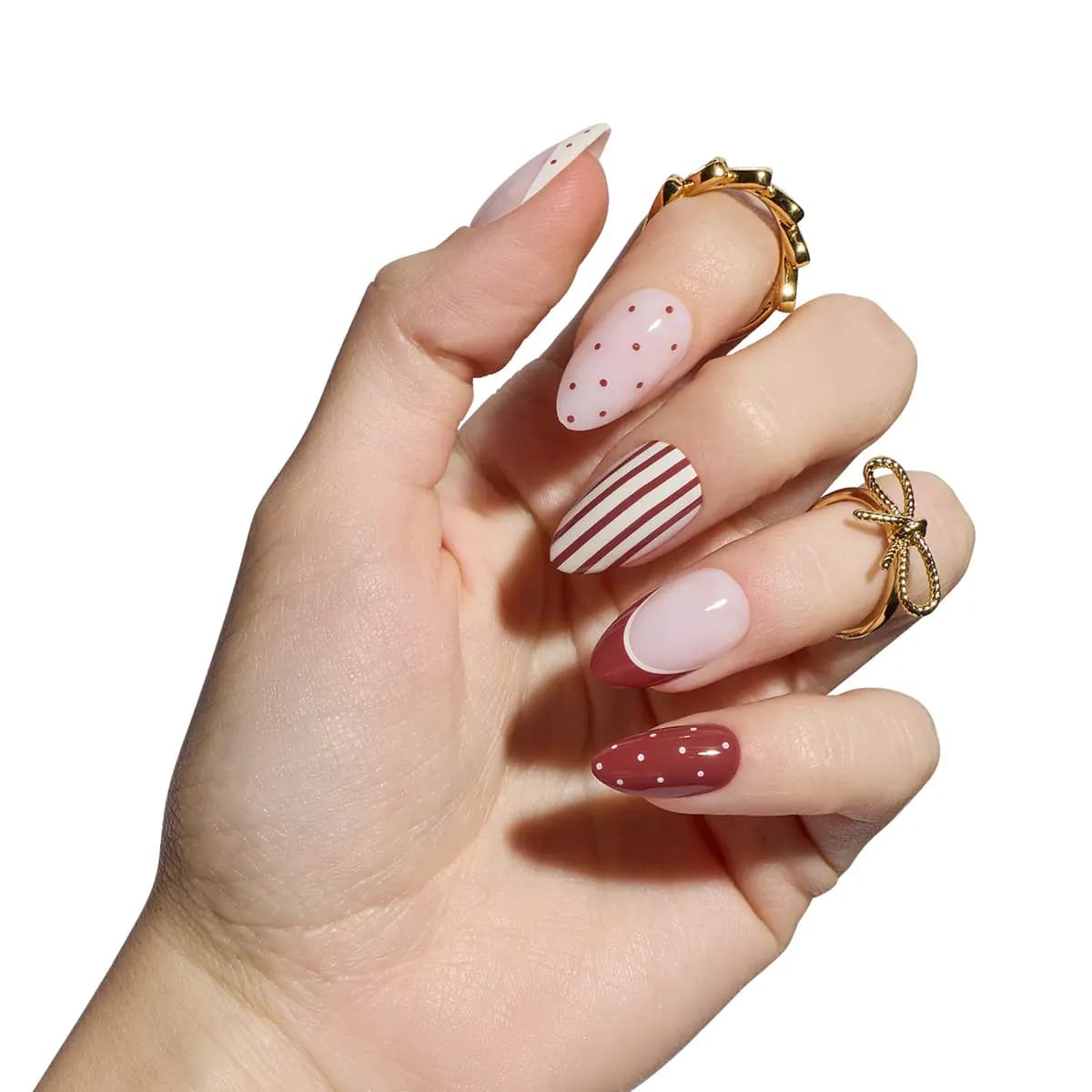 Hand wearing Cocoa Muse short almond press-ons: cocoa stripes, dots and French tips on blush nude, with gold rings.