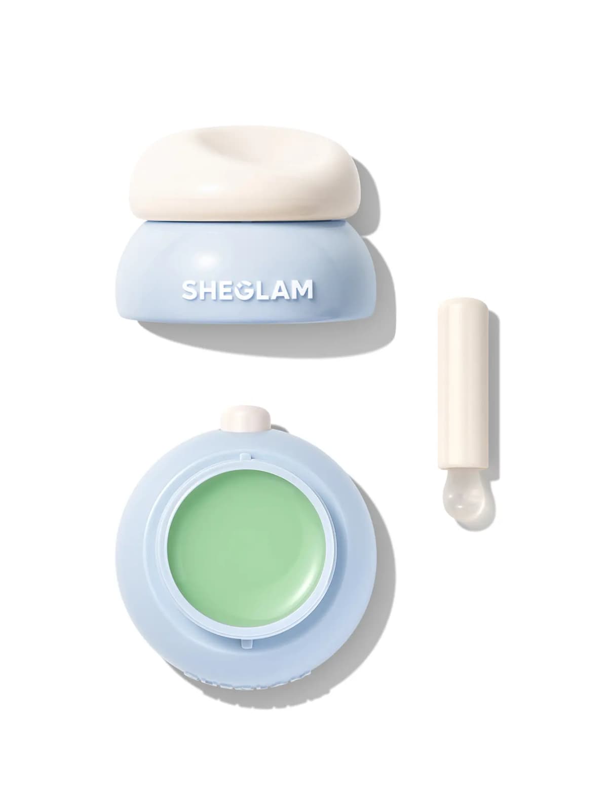 Blue jar with cream lid, open pan of mint green lip mask and white silicone-tipped applicator on white