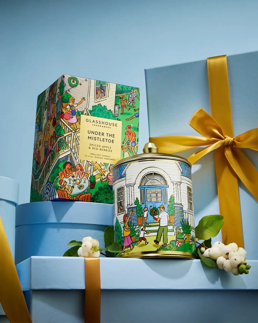 Glasshouse Under the Mistletoe candle tin showing a white house with blue door, beside its garden-party box and snowberries