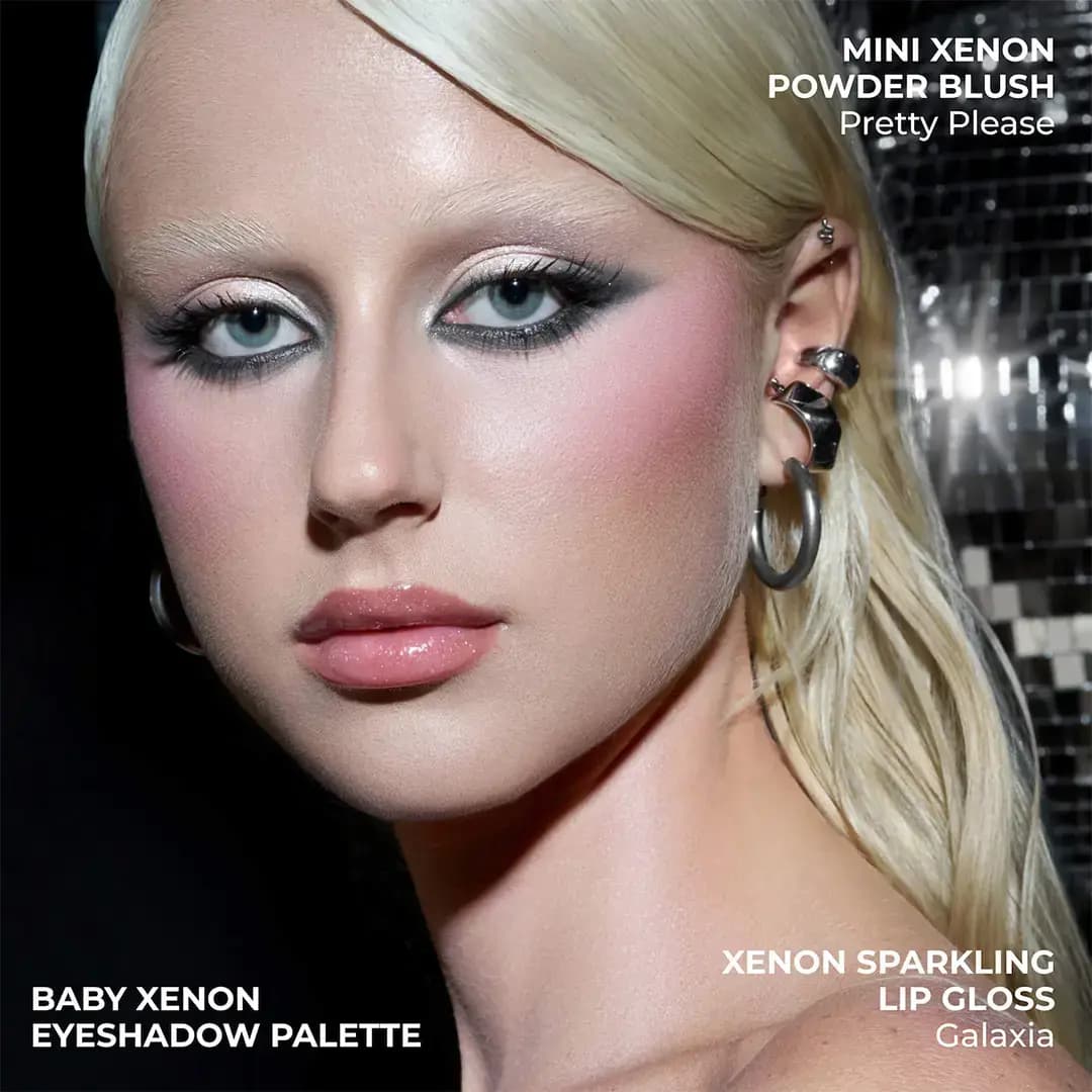 Blonde model with grey winged smoky eyes, pink blush and glossy lips before a mirrored disco backdrop, Xenon set shades.