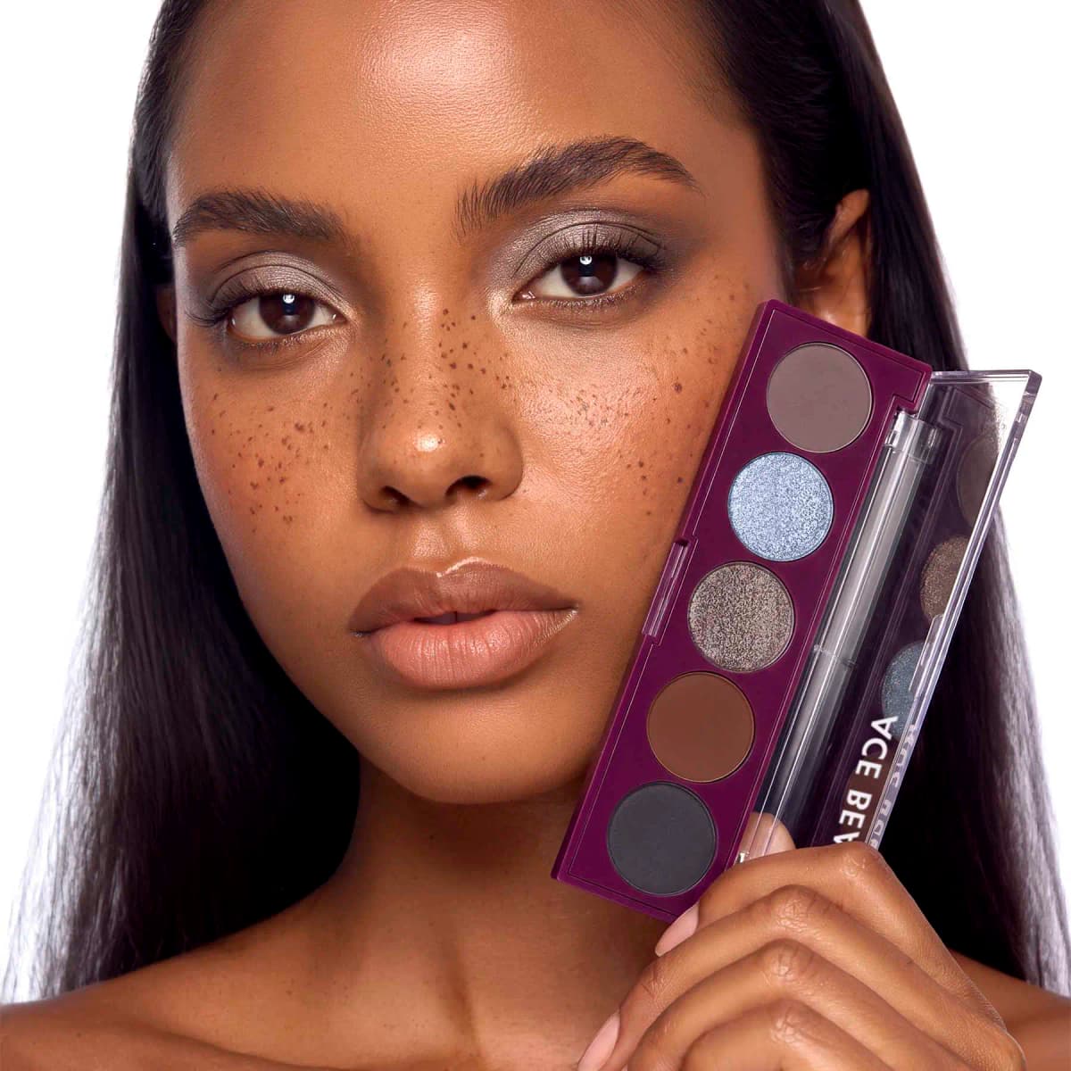 Freckled model with soft taupe shimmer eyes holding the open plum Ace Beauté Mini Serenade palette against her cheek.