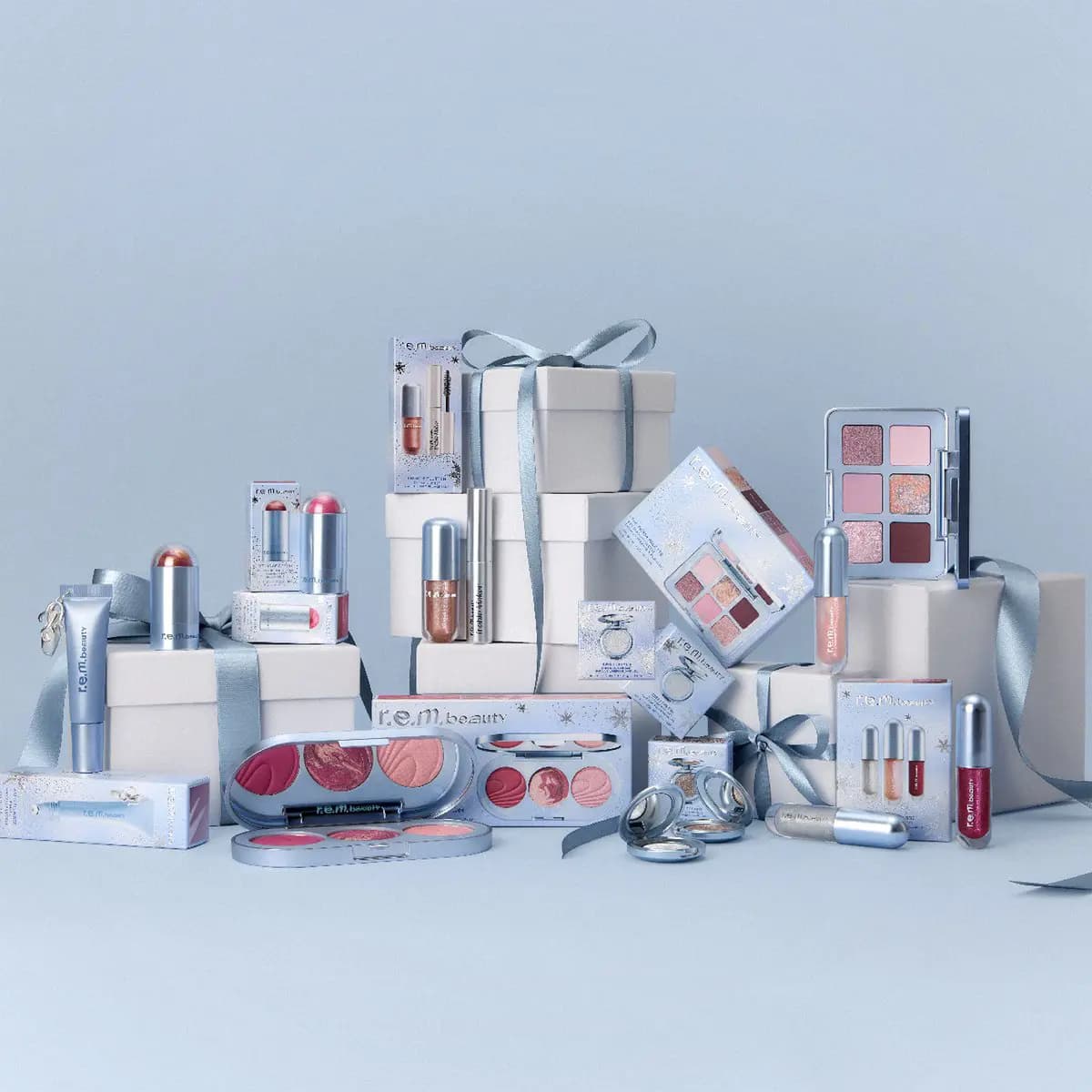 R.e.m. beauty holiday collection of palettes, lip glosses, mascaras and sticks arranged with white gift boxes