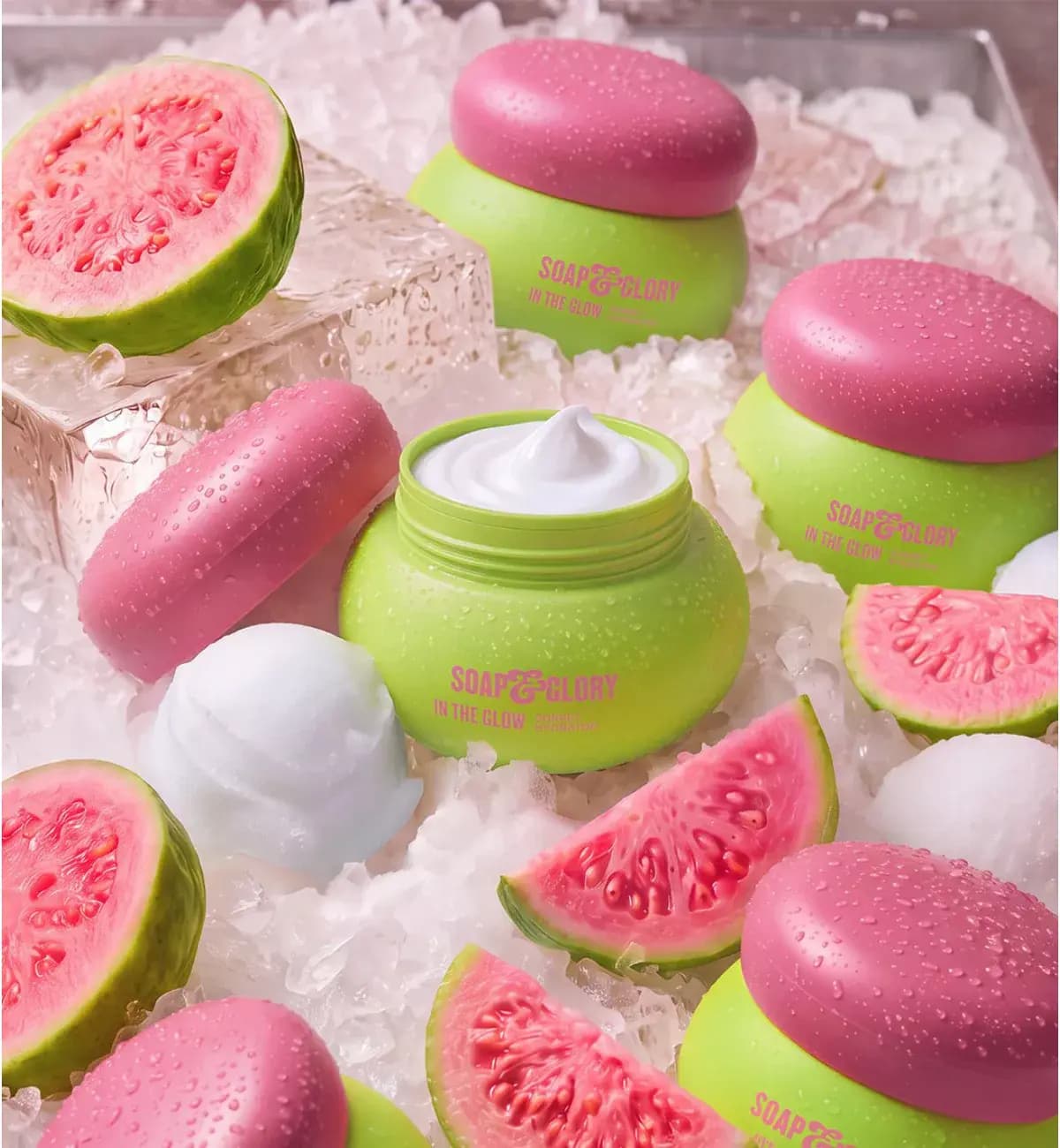 Lime green In The Glow Sorbet Hydrator jars with pink lids, one open, on crushed ice with sliced guava
