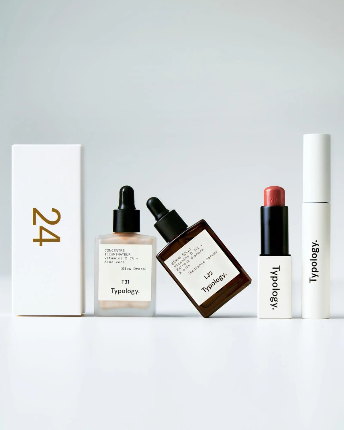 Gold-numbered 24 box beside Typology Glow Drops T31, Radiance Serum L32, a tinted lip balm and a white tube.