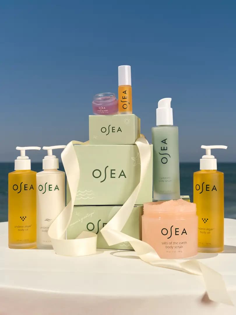 OSEA From Malibu to You Holiday 2026 gift sets: body oils, lotion, serum, scrub and lip care on green boxes by the sea
