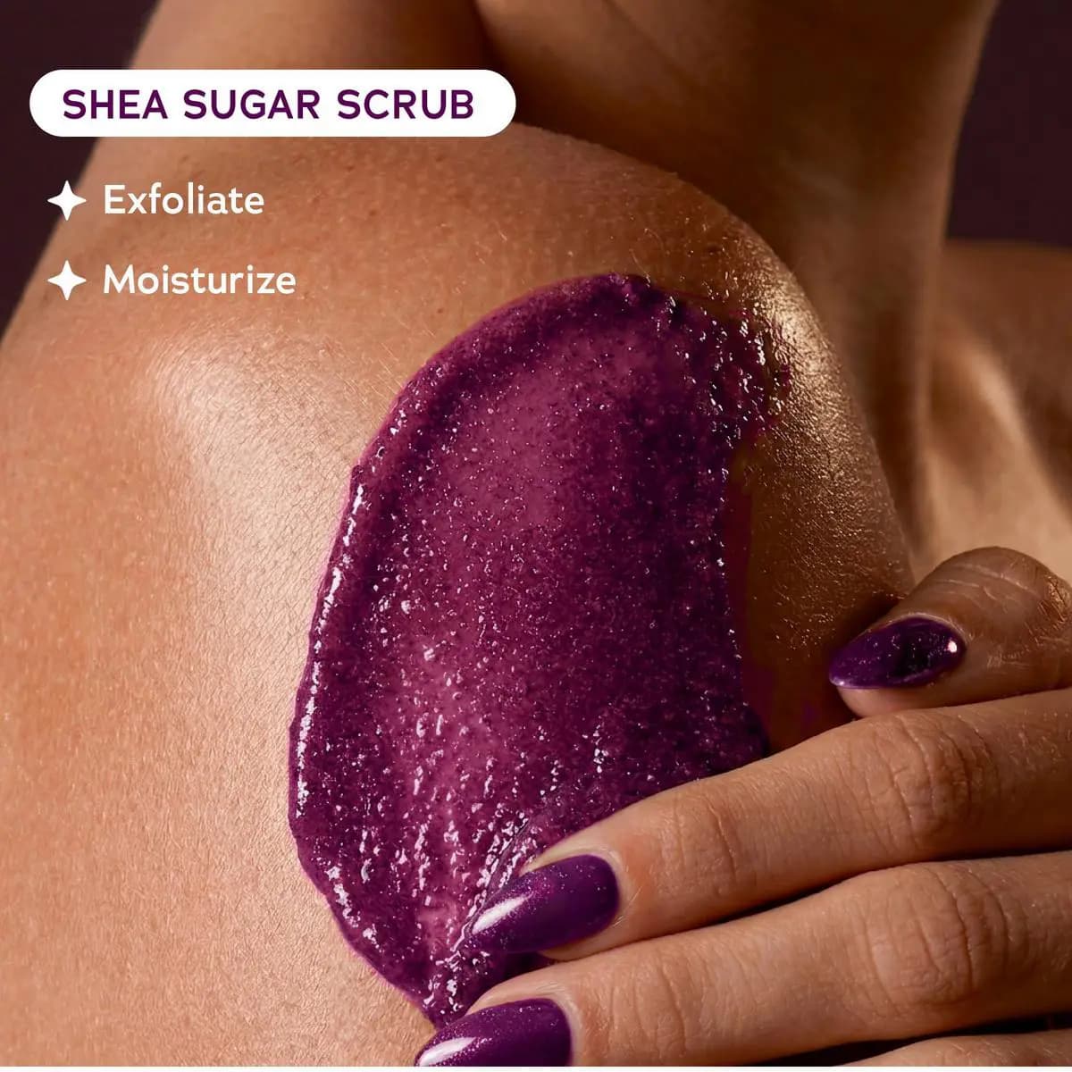 Close-up of deep purple sugar scrub swatch being massaged onto a shoulder with text Exfoliate and Moisturize