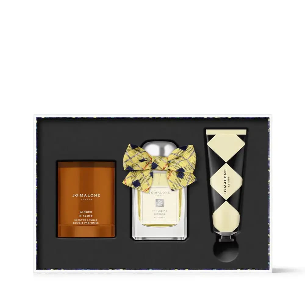 Black gift set tray holding a Ginger Biscuit candle, bowed Tangerine & Honey cologne and harlequin-print hand cream