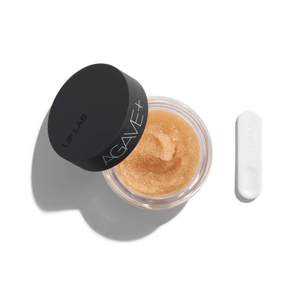 Open Lip Lab Agave+ Lip Scrub jar showing golden sugary scrub, black lid and white spatula on a white background