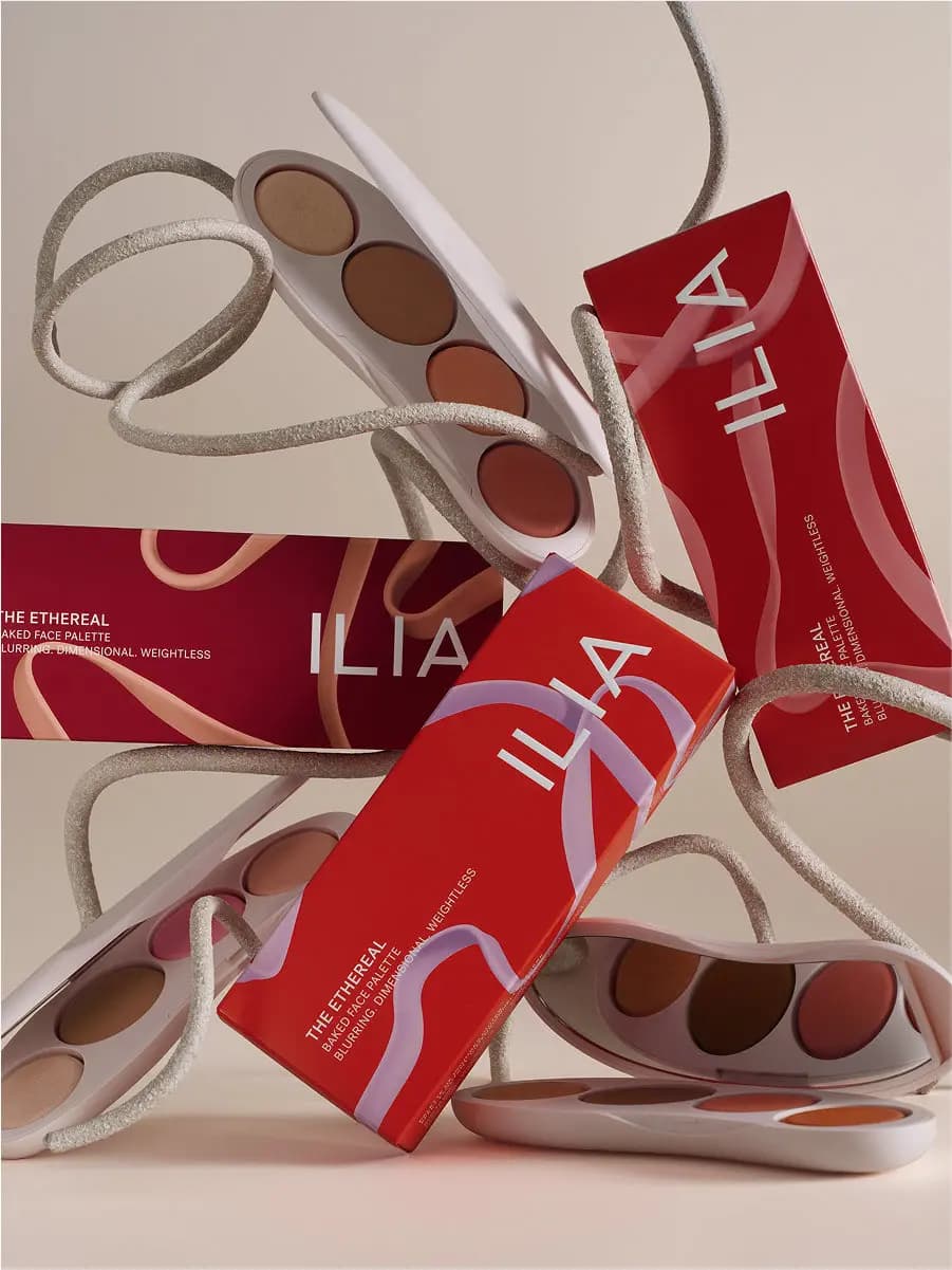 Three Ilia Ethereal Baked Face Palettes in red and burgundy packaging arranged with beige ribbon on a neutral backdrop