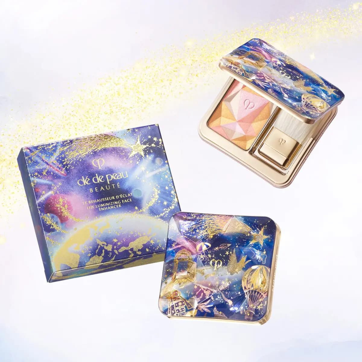 Clé de Peau Beauté Luminizing Face Enhancer box, open compact and starry illustrated lid floating on a gold-dusted sky