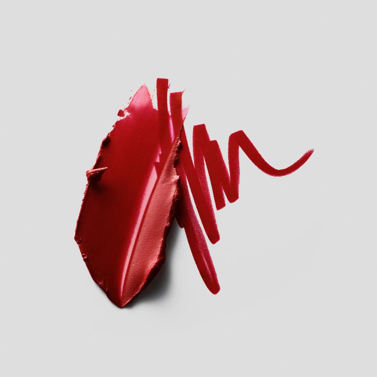 Smeared red lipstick swatch beside zigzag strokes of a matching red lip liner on grey