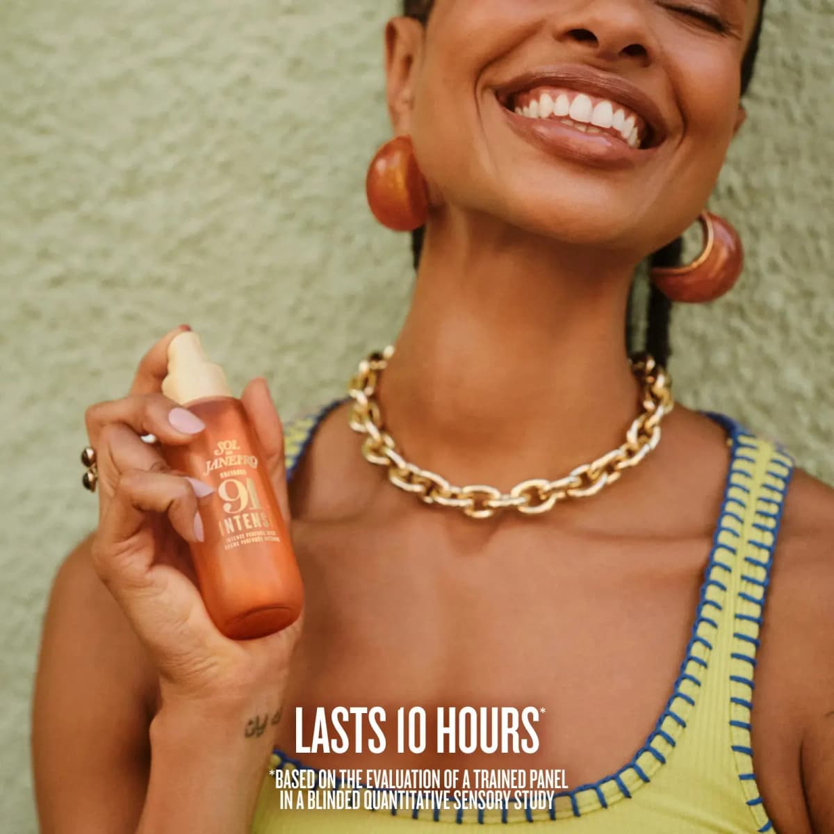 Smiling woman in a gold chain necklace holding the uncapped bottle, with the text "Lasts 10 Hours"