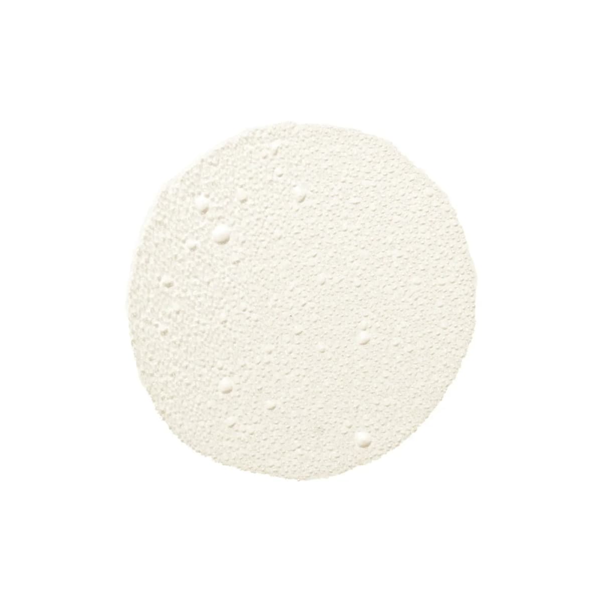 Round swatch of milky white liquid with tiny droplets and bubbles across the surface.