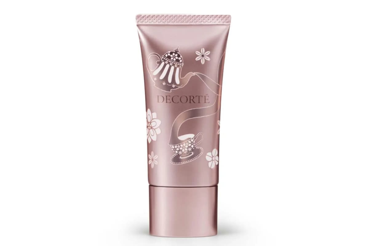 Rose-gold DECORTÉ primer tube decorated with a white teapot pouring into a teacup and flowers