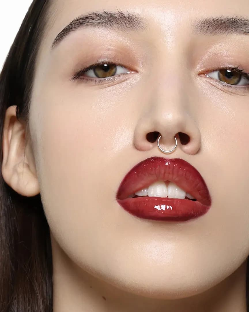 Model with septum ring wearing a glossy burgundy ombré lip with dark lined edges and lighter centre