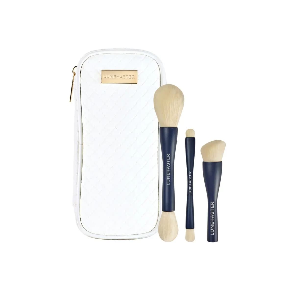 White quilted Lune+Aster zip case with gold plaque beside three navy-handled double-ended makeup brushes