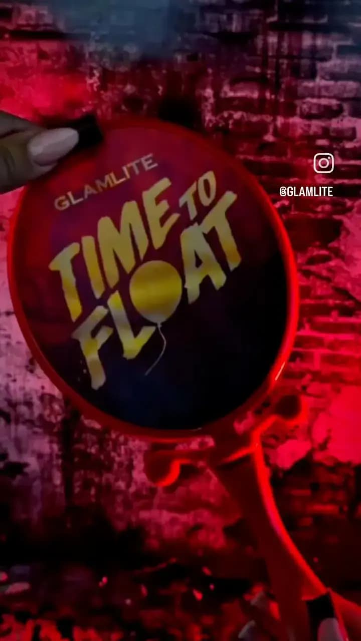 Back of the red mirror showing gold Glamlite 'Time to Float' text with a balloon motif against a red brick wall