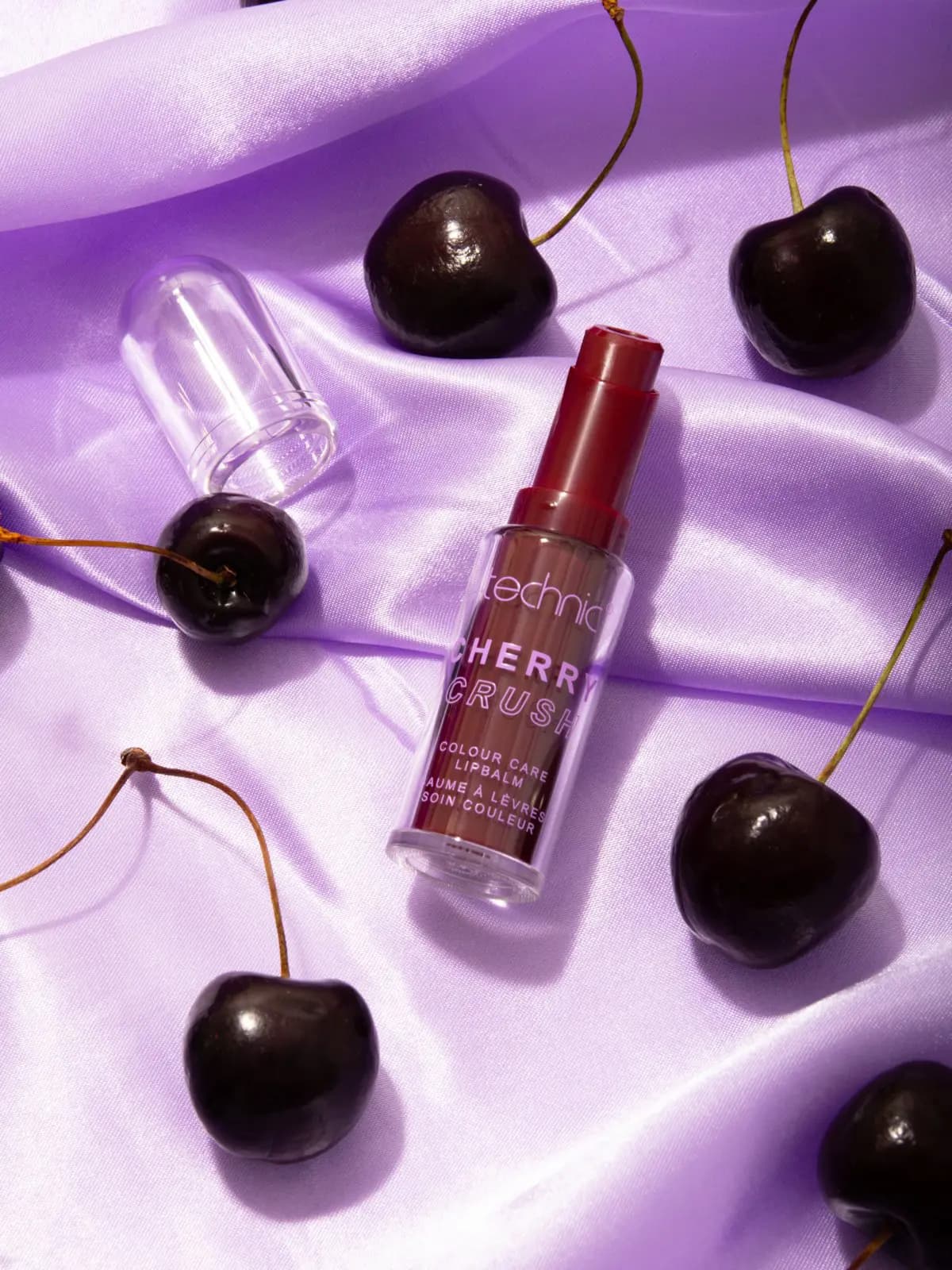 Uncapped Cherry Crush colour care lip balm in deep red on lilac satin surrounded by dark cherries