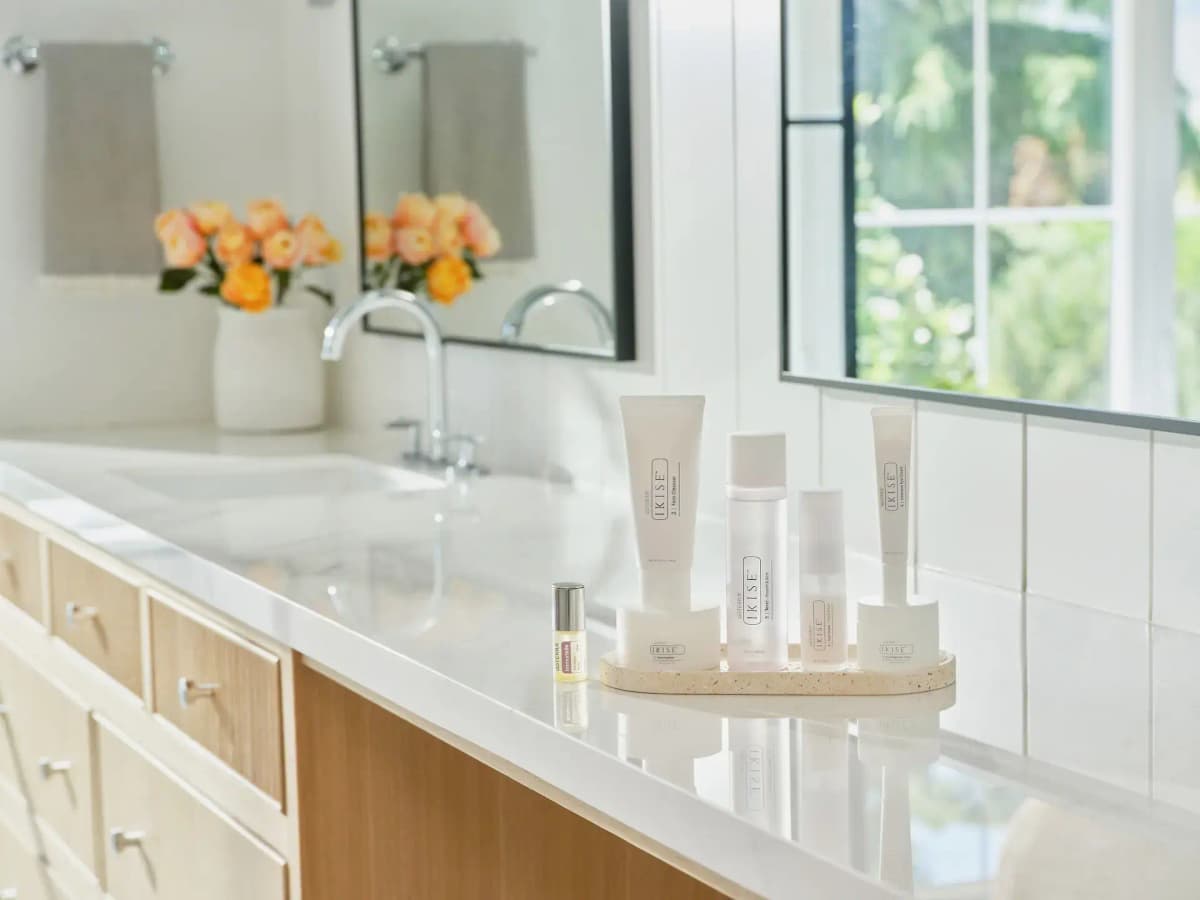 DōTERRA IKISE Skincare Collection on a speckled tray with Immortelle roller on a white bathroom vanity by a sunny window