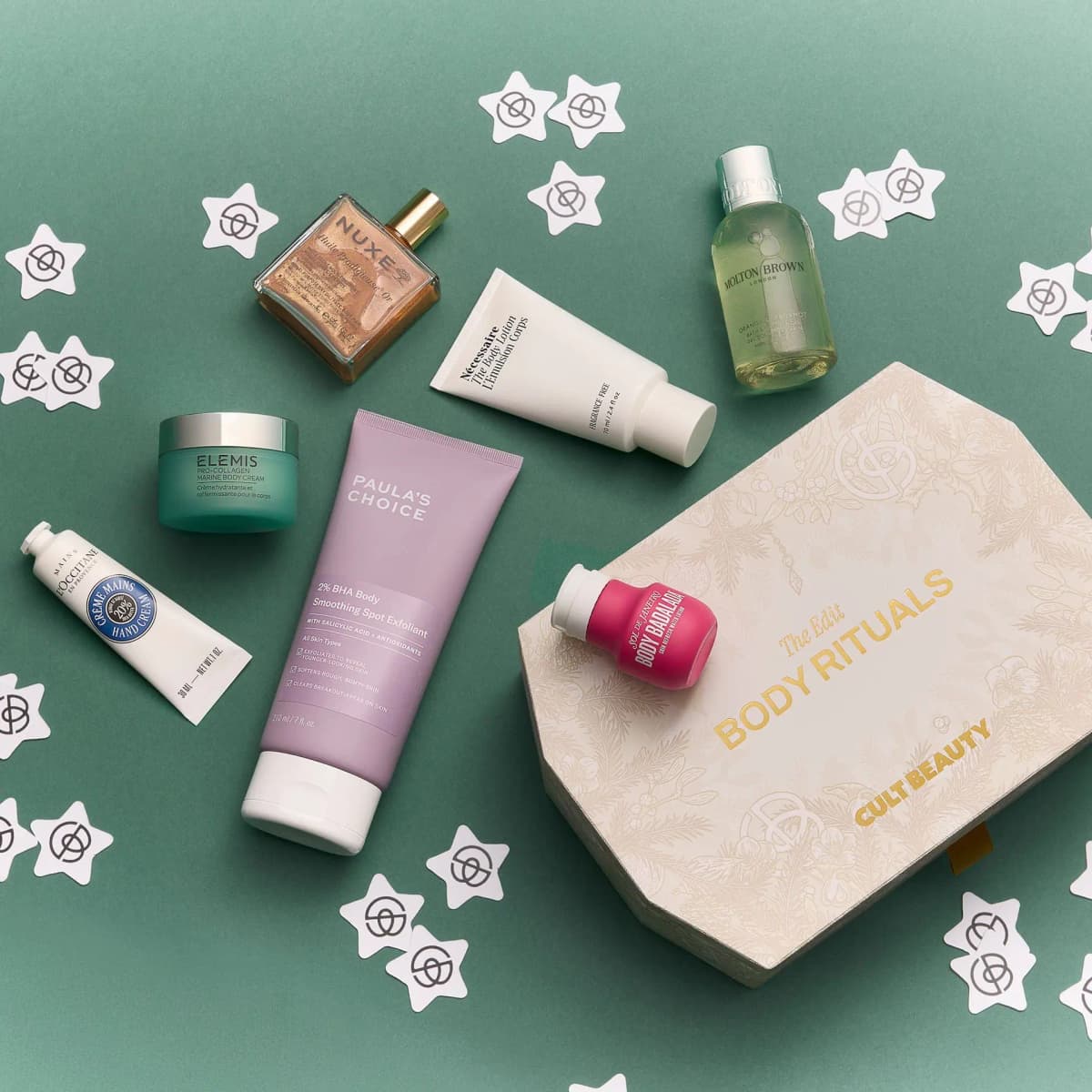 Flat lay of Body Rituals box on green with NUXE oil, Paula's Choice exfoliant, Elemis cream and Sol de Janeiro