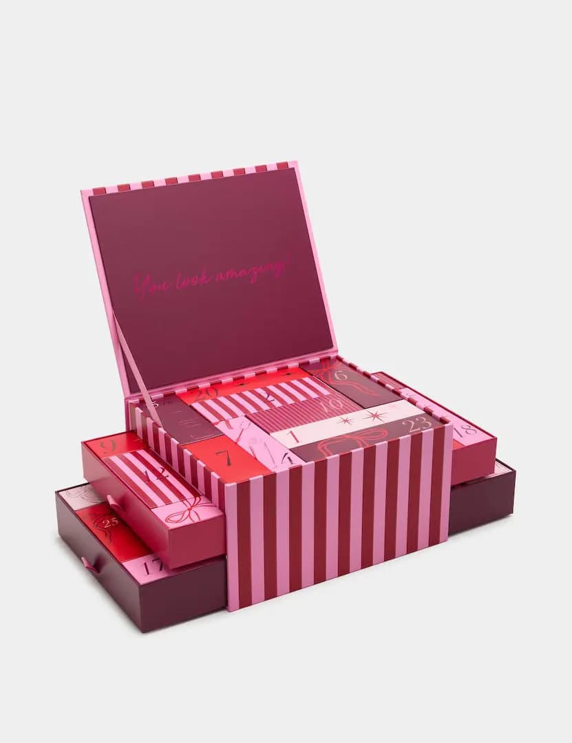 Open red-and-pink striped advent box reading 'You look amazing!' with numbered doors and pull-out drawers
