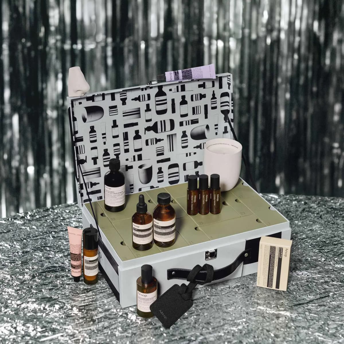 Aesop Valise advent calendar open on silver surface with numbered drawer inserts and products arranged around it.