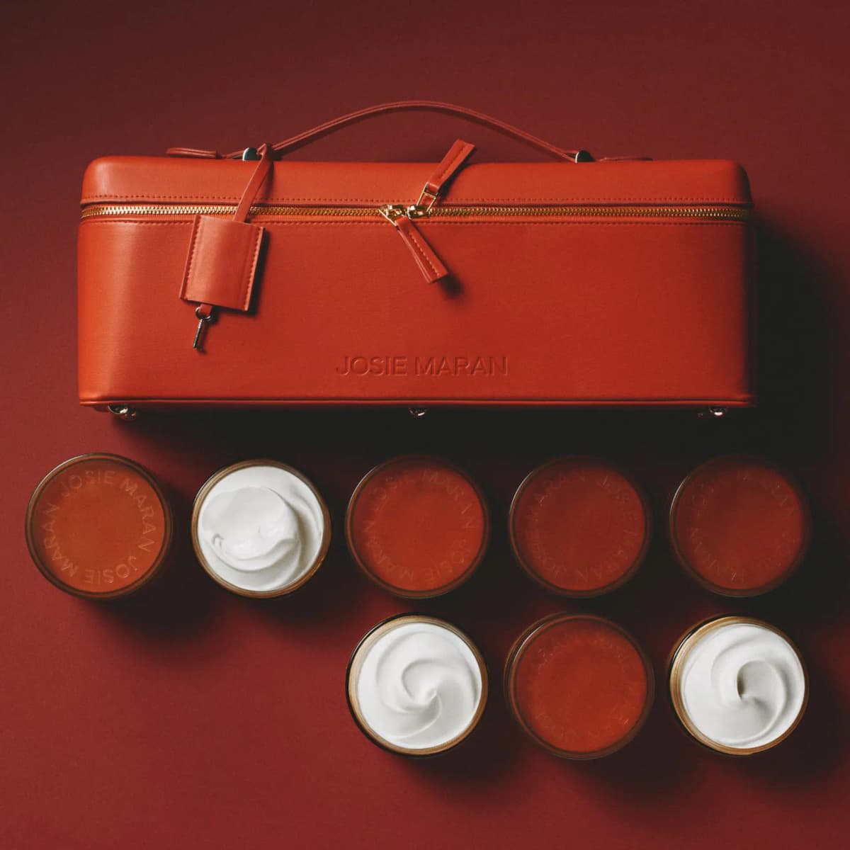 Overhead view of the red Josie Maran train case above eight amber jars, three open to show white whipped butter