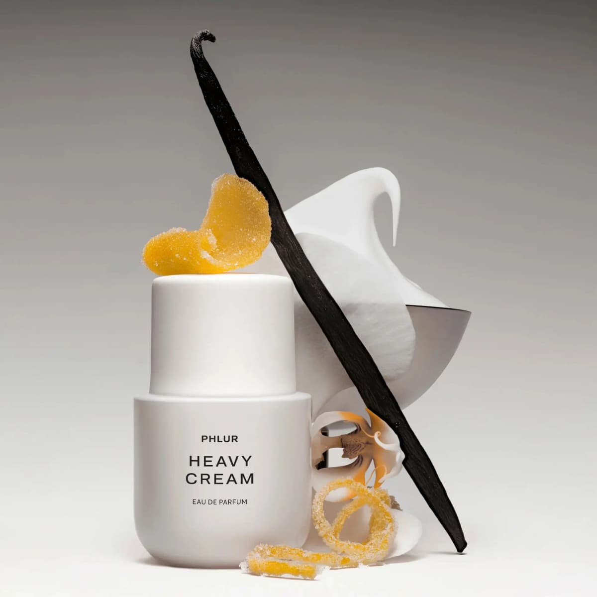 PHLUR Heavy Cream bottle styled with a vanilla pod, sugared citrus peel, a white orchid and whipped cream in a bowl