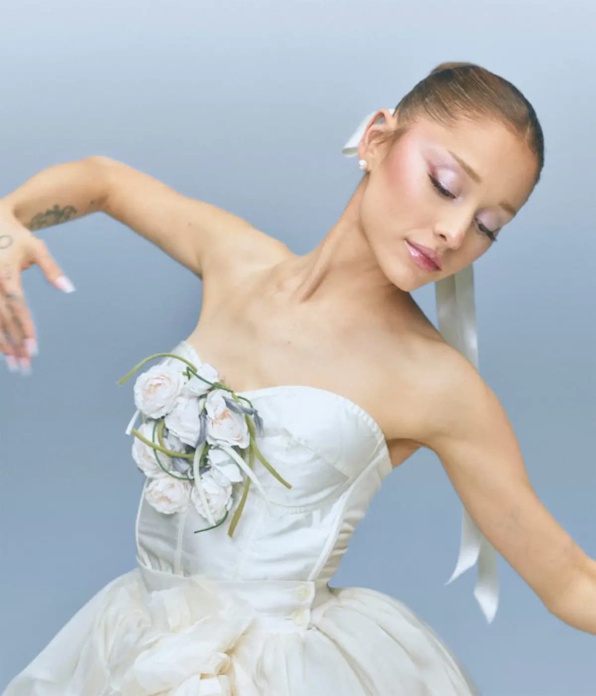 Model with sleek bun, pink shimmer eyes and glossy lips poses like a ballerina in a white strapless gown with roses