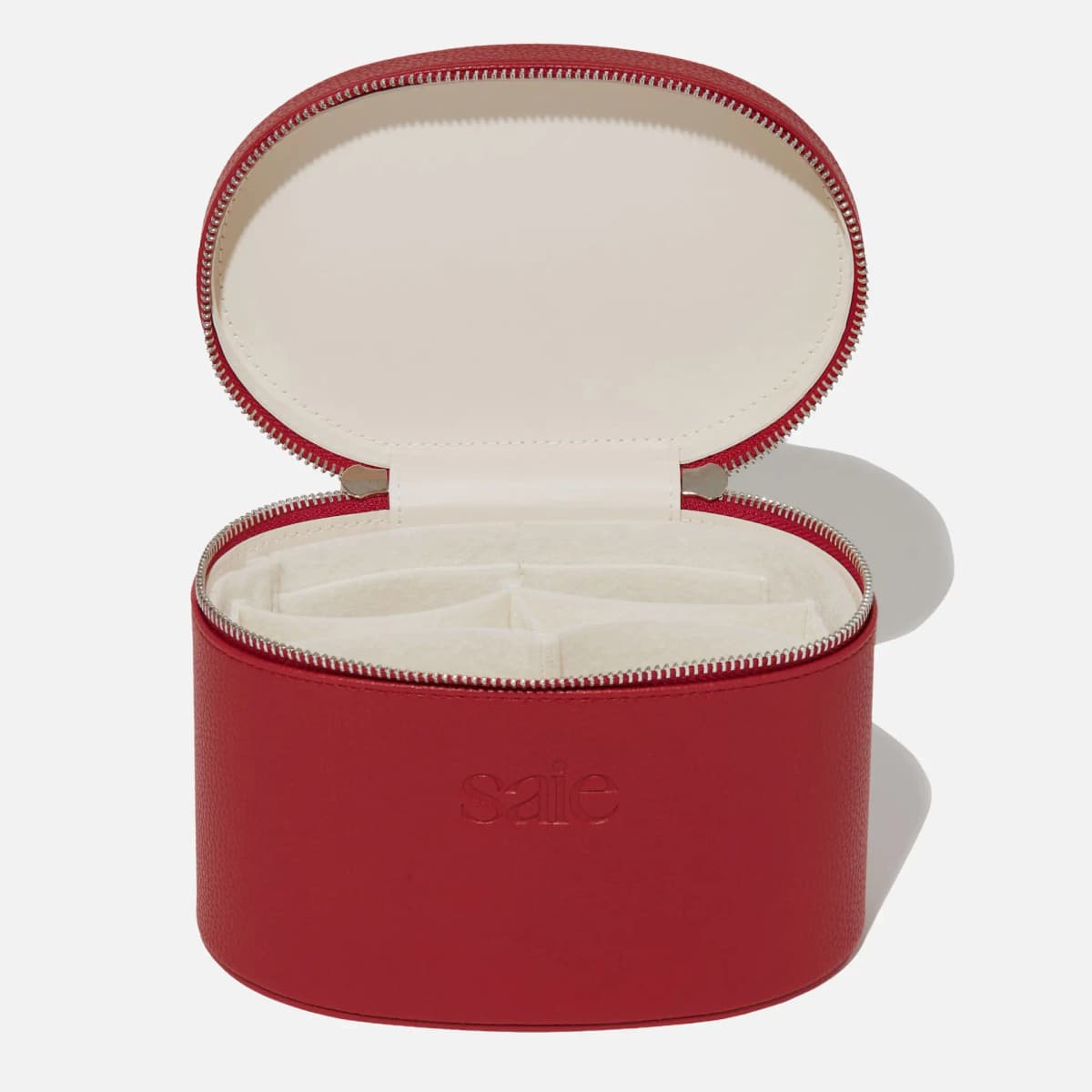 Red Saie vanity case unzipped to show a cream lining and felt compartment dividers inside