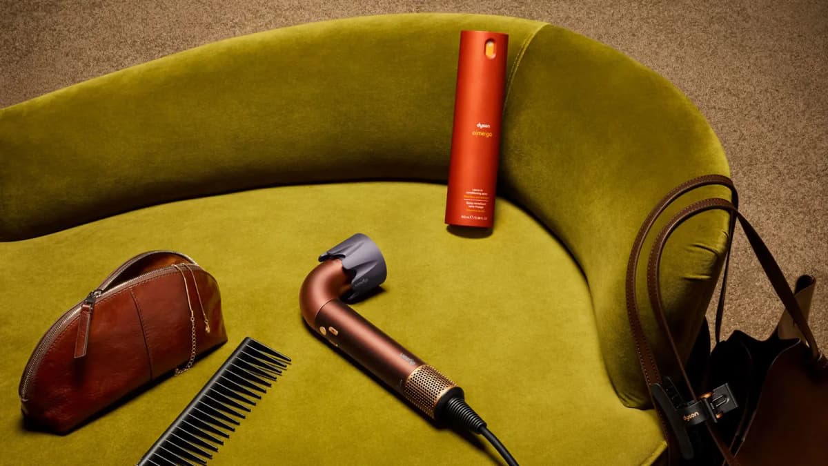 L-shaped copper hair dryer on an olive velvet sofa with an orange Dyson o|me|ga conditioning spray, comb and leather pouch