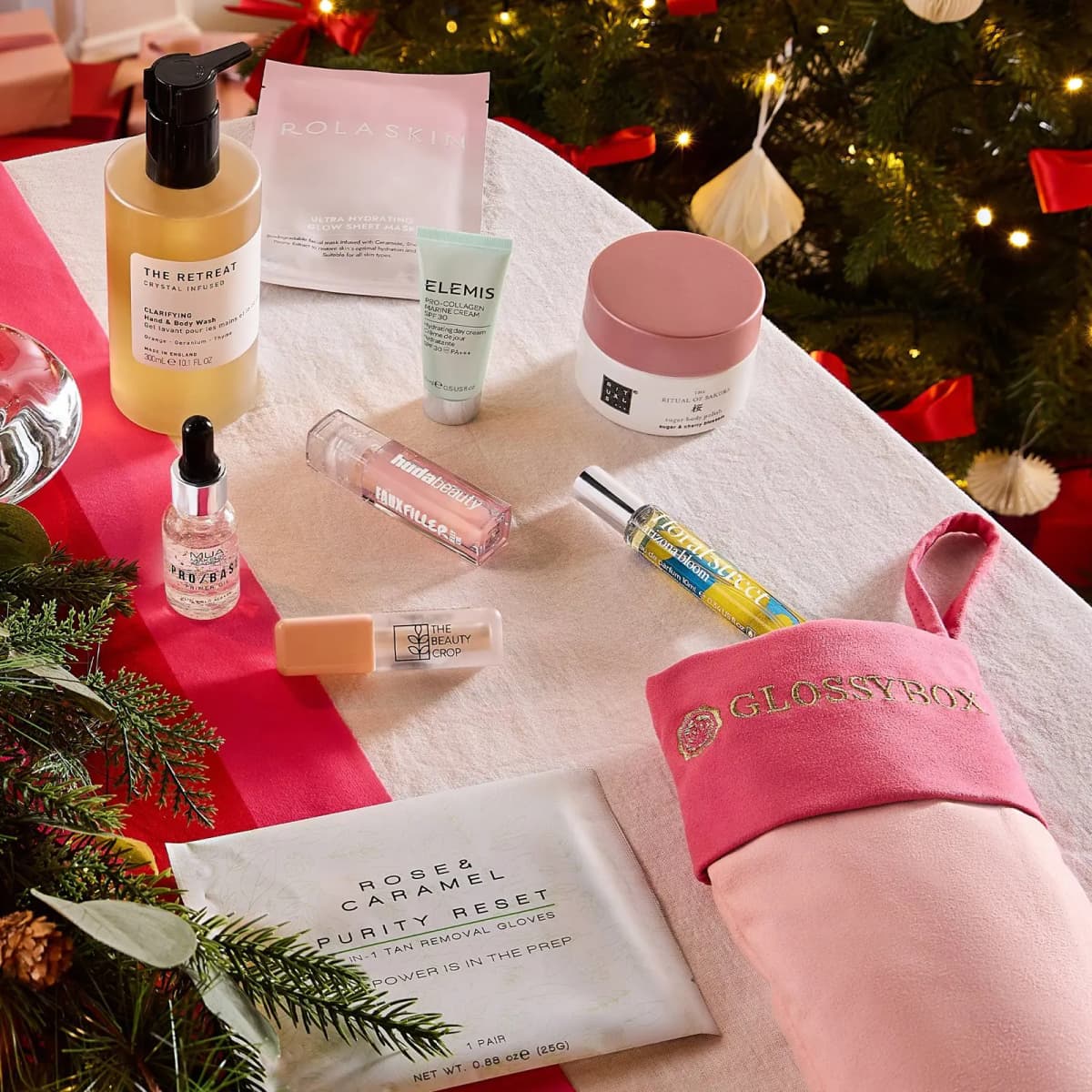 Stocking items incl. Elemis cream, Huda Beauty lip gloss and Floral Street perfume on a festive table with pink stocking