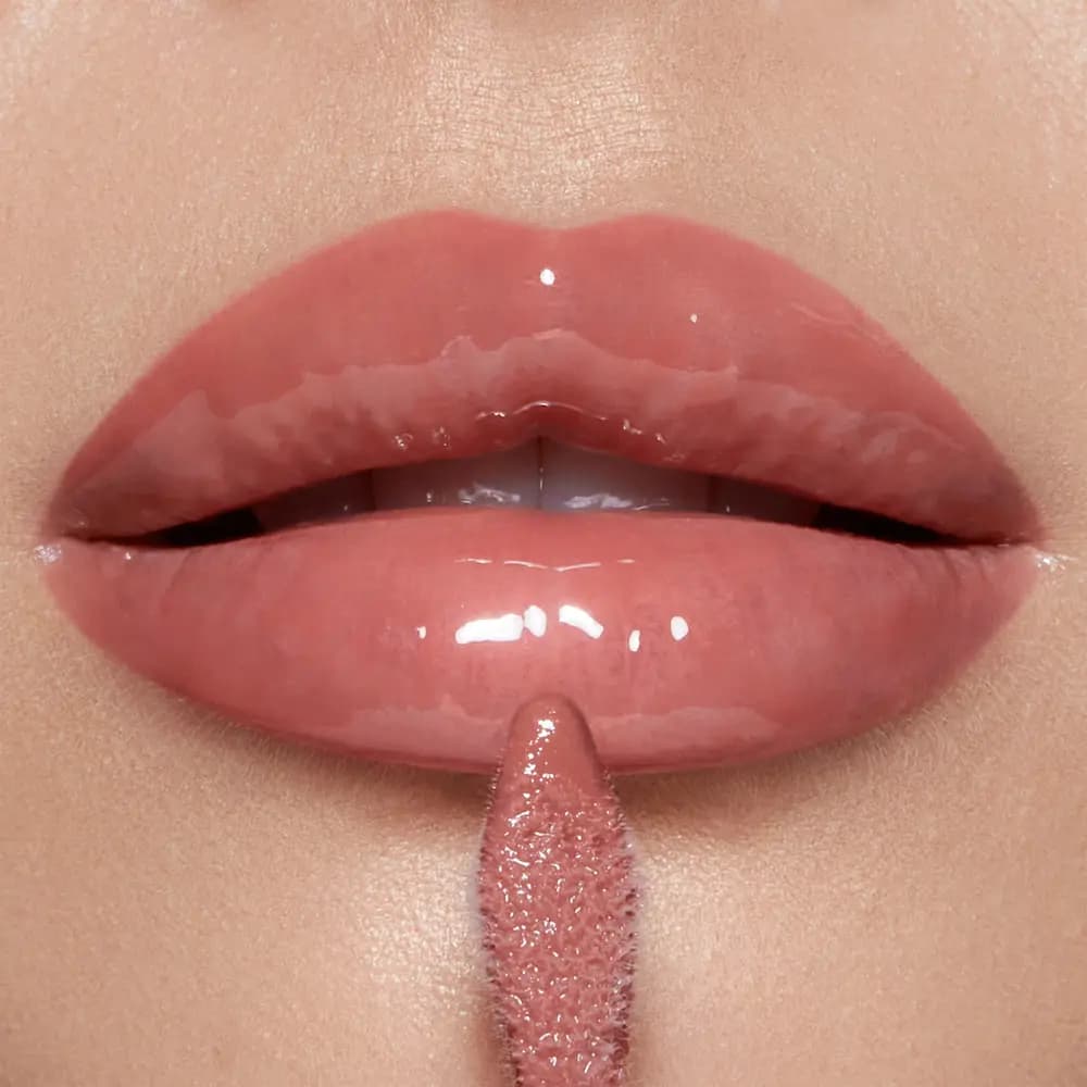 Close-up of glossy rosy nude lips with a doe-foot gloss applicator held below the lower lip