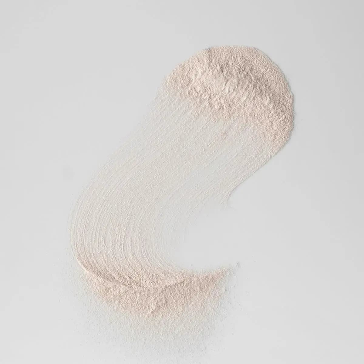 Swipe of fine pale beige powder spread in a curved stroke across a light grey surface