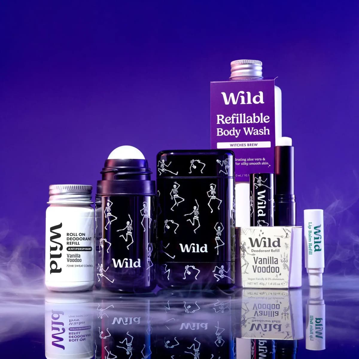 Wild Witches Brew Refillable Body Wash with skeleton cases, Vanilla Voodoo refills and lip balm on a reflective purple set