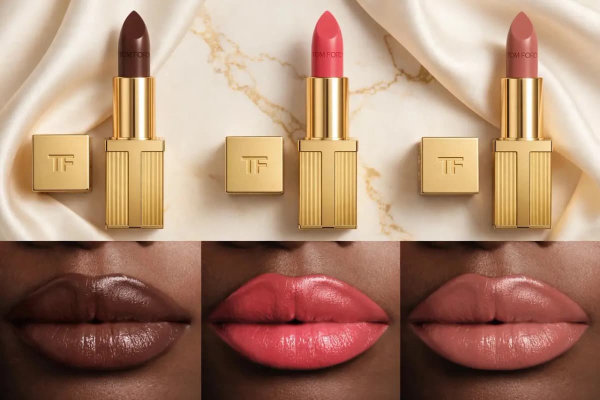 Three gold Tom Ford lipsticks in brown, coral and nude on marble above matching glossy lip swatches on deep skin