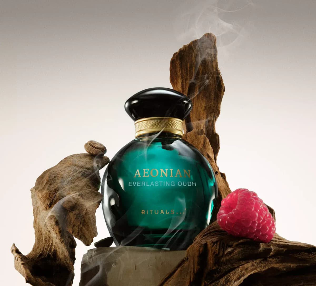 Rituals Aeonian Everlasting Oudh in a dark teal bottle with black cap among smoking oud wood, a coffee bean and a raspberry