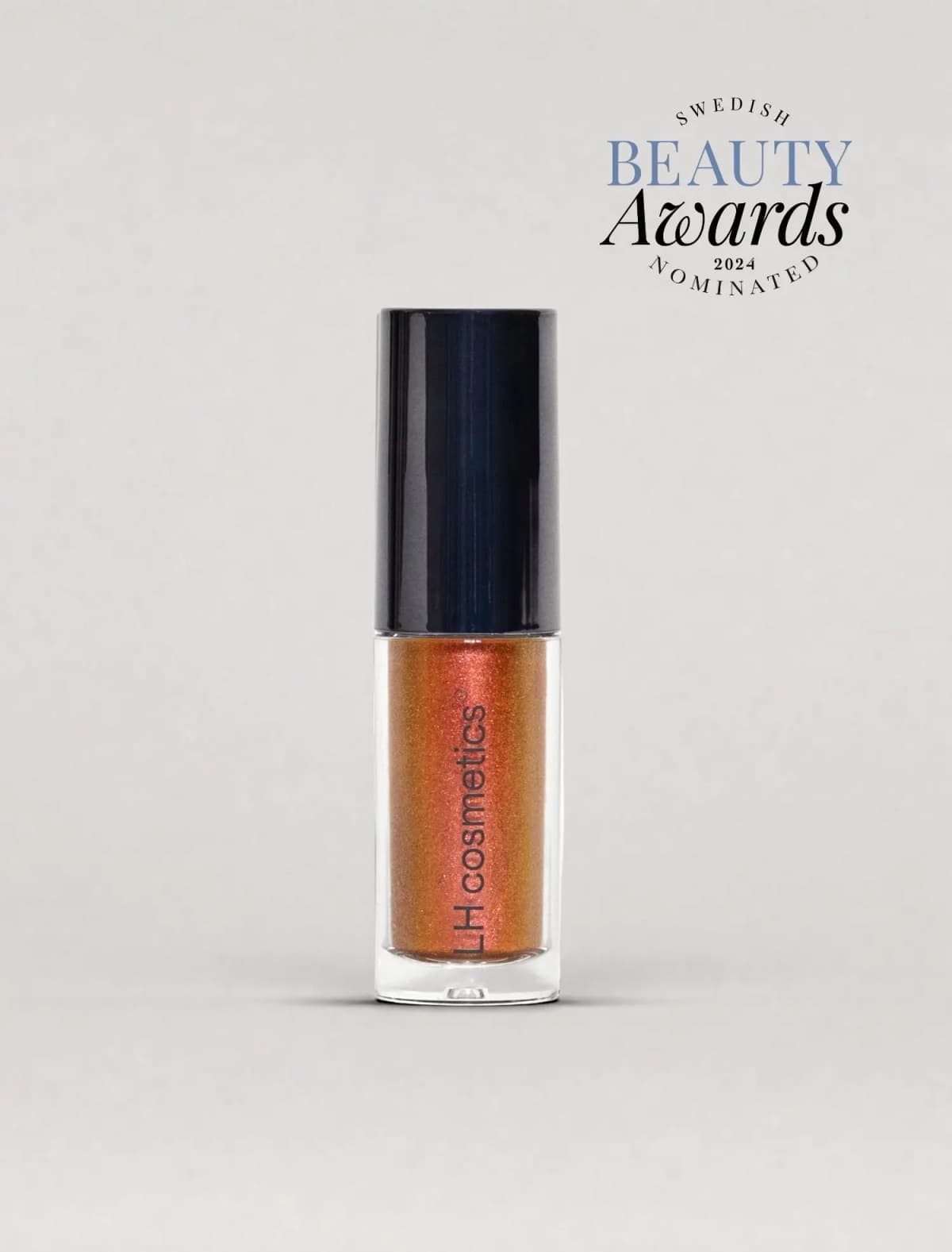 Clear eyeshadow tube with black cap filled with copper-red shimmer, beside a Swedish Beauty Awards 2024 nominee badge