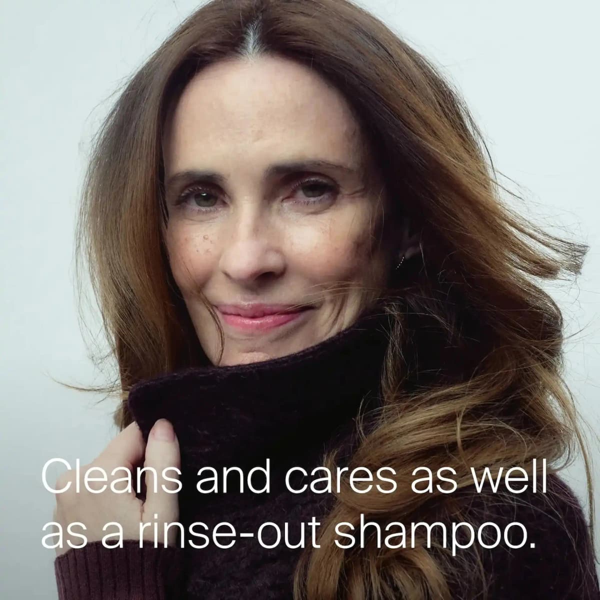 Smiling woman with glossy, voluminous brown hair tucking her chin into a dark plum turtleneck, with cleansing claim text