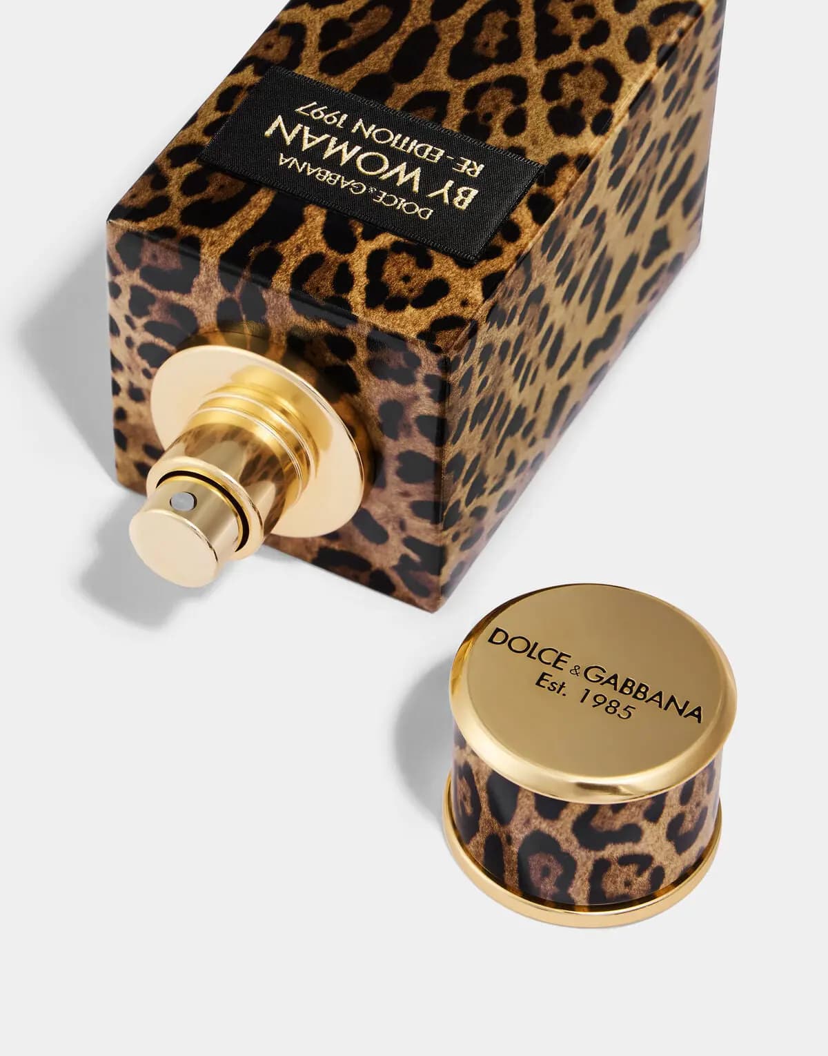 Uncapped leopard-print By Woman bottle showing the gold sprayer, beside a gold cap engraved "Dolce&Gabbana Est. 1985"