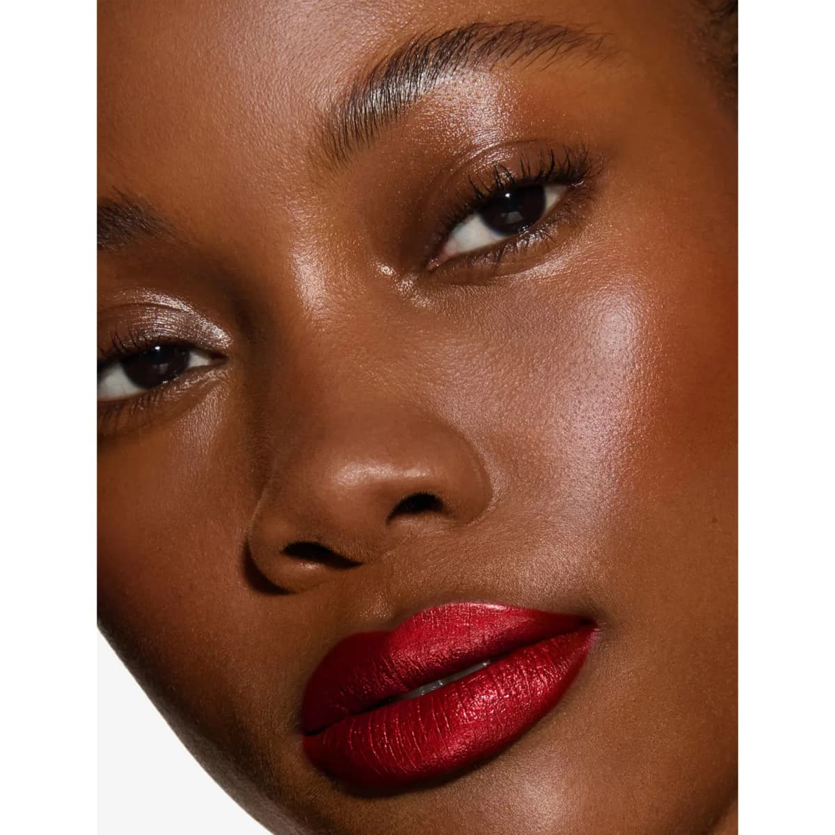 Close-up of a deep-skinned model wearing a pearlised deep red lipstick with luminous skin